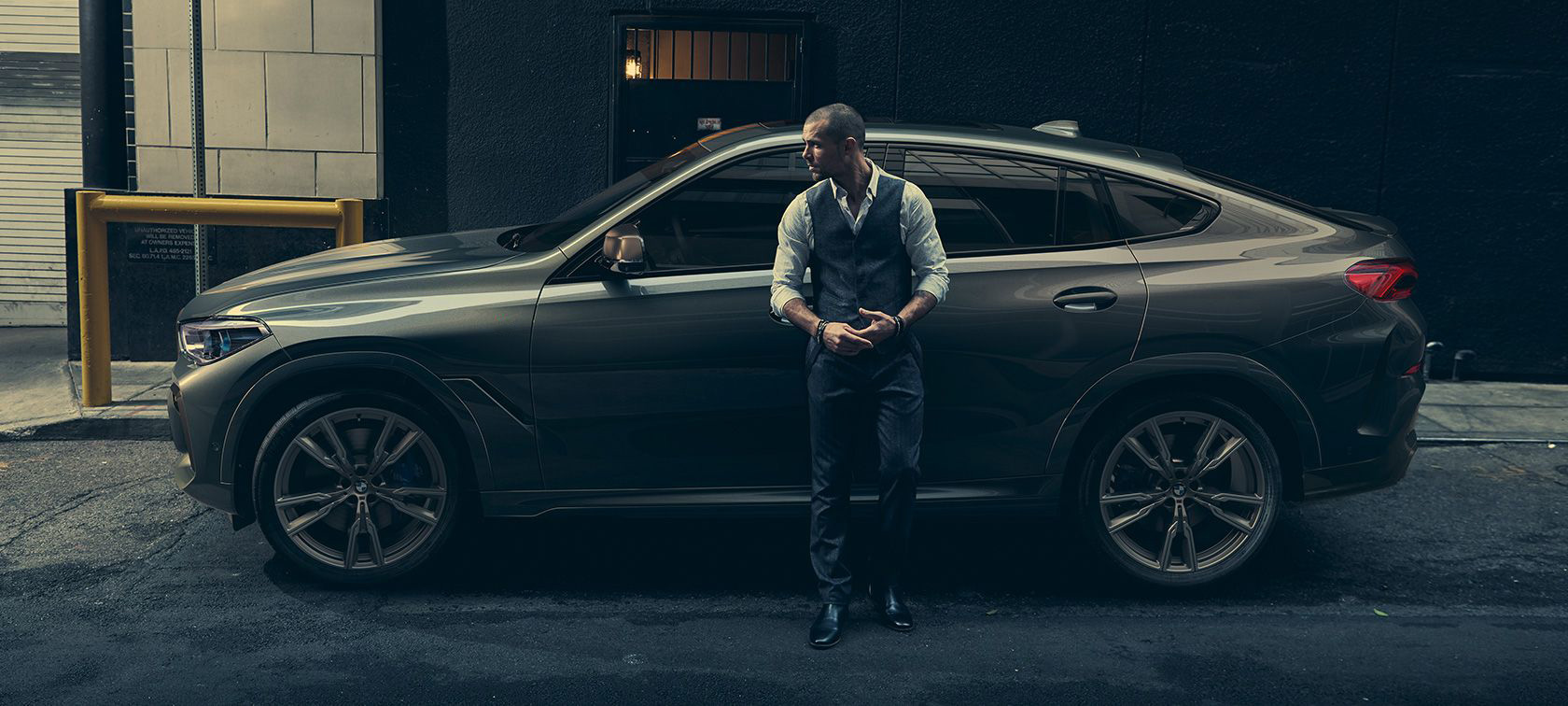 Man leaning on BMW X6. Man leaning on BMW X6 in lateral perspective in front of an urban setting.